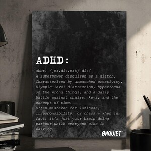 Op de afbeelding: Een zwart-wit print met het woord "ADHD" in grote witte letters. De tekst eronder definieert ADHD als een superkracht vermomd als een glitch. De print staat op een bureau met een zwarte mok, pennen en notitieboeken.