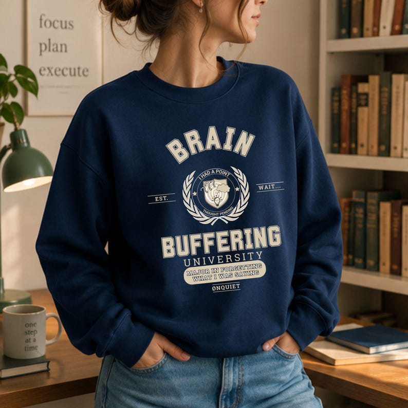 Może przedstawiać: Granatowa bluza z okrągłym dekoltem i kremową grafiką z napisem BRAIN BUFFERING UNIVERSITY, EST. WAIT, I HAD A POINT THOUGHT PENDING, MAJOR IN FORGETTING WHAT I WAS SAYING oraz ONQUIET, umieszczonym centralnie wok&oacute;ł okrągłego emblematu.