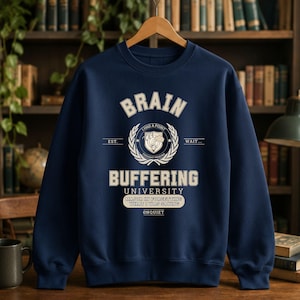 Może przedstawiać: Granatowa bluza z okrągłym dekoltem i kremowym nadrukiem z napisem BRAIN BUFFERING UNIVERSITY. Projekt zawiera centralny emblemat z tekstem I HAD A POINT THOUGHT PENDING oraz baner z napisem MAJOR IN FORGETTING WHAT I WAS SAYING.