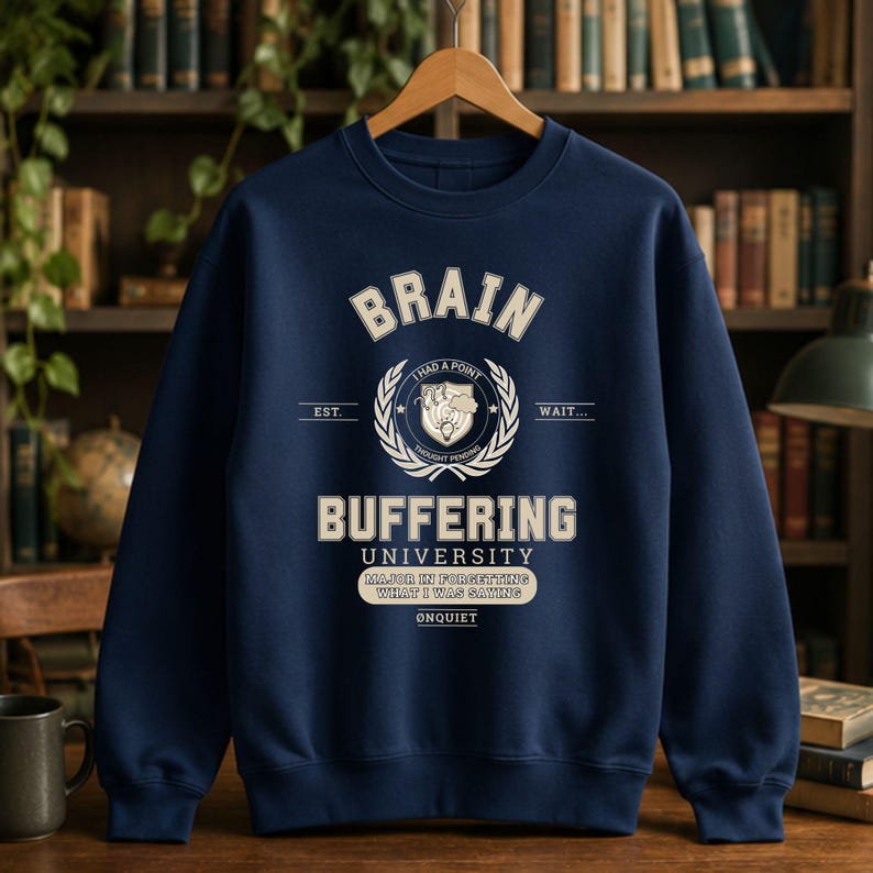 Może przedstawiać: Granatowa bluza z okrągłym dekoltem i kremowym nadrukiem z napisem BRAIN BUFFERING UNIVERSITY. Projekt zawiera centralny emblemat z tekstem I HAD A POINT THOUGHT PENDING oraz baner z napisem MAJOR IN FORGETTING WHAT I WAS SAYING.