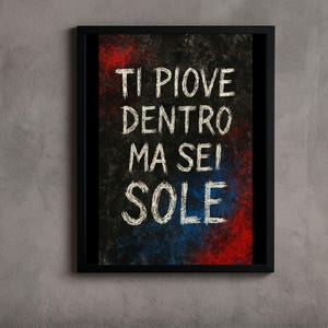 May include: Framed art print with the Italian phrase "Ti Piove Dentro Ma Sei Sole" in white chalk-style lettering on a textured black background with red and blue accents. The black frame adds a modern touch.