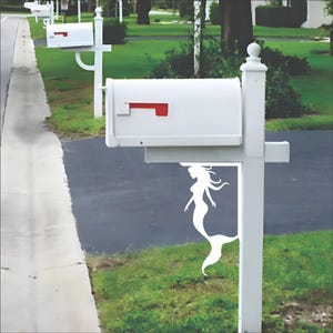 May include: White mailbox with a red flag and a decorative mermaid cutout. The mailbox is mounted on a white post. Several mailboxes are visible along a residential street.