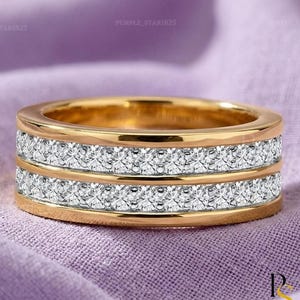May include: A gold band ring featuring two parallel rows of small, clear, round-cut stones set into the metal. The ring has a polished gold finish on the top and bottom edges, framing the two horizontal channels of sparkling white stones.