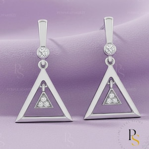 May include: A pair of silver-toned earrings with a geometric design. Each earring features a triangle shape with a smaller triangle inside, adorned with small, sparkling stones. A round stone is set at the top of each earring.