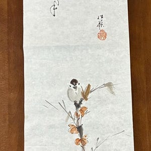 以下が含まれることがあります： 花咲く枝に止まる鳥を描いた縦長の巻物。墨絵で描かれ、繊細な筆致でミニマルな美しさを表現。書と赤い印章も含まれています。