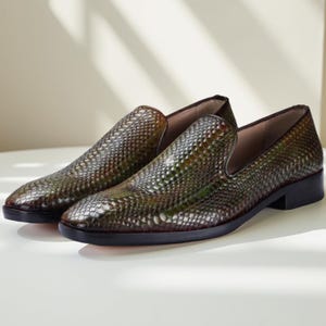 Puede incluir: Un par de mocasines de cuero texturizado marrón y verde. Los zapatos tienen un diseño sin cordones con un tacón bajo y una punta redondeada. El cuero tiene un patrón de escamas y las suelas son negras.