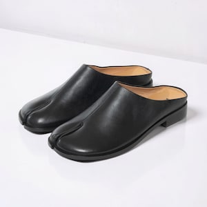 May include: A white ceramic mug with a black handle and the text "But First, Coffee" in a bold, black font. The mug is set against a blurred background, suggesting a cozy setting.