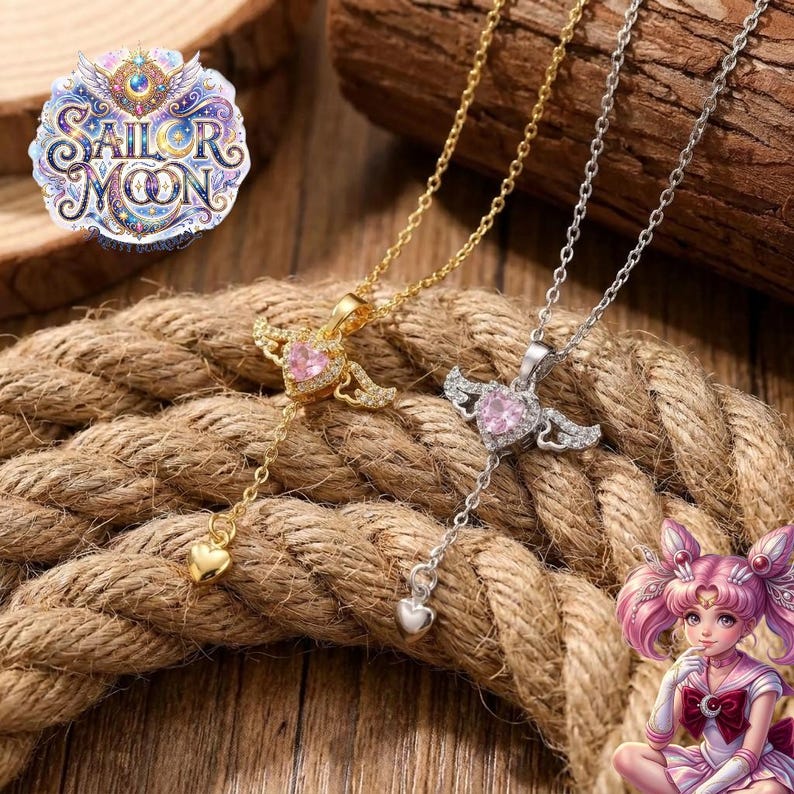 Puede incluir: Dos collares con una piedra preciosa rosa en forma de coraz&oacute;n flanqueada por peque&ntilde;as alas y un dije de coraz&oacute;n colgante en la parte inferior. Un collar es dorado y el otro plateado. El logotipo de Sailor Moon es visible en la esquina superior.