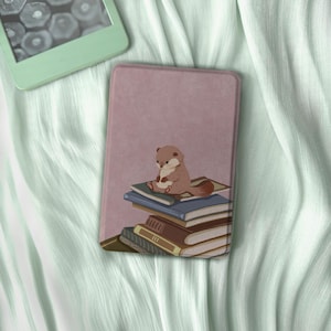 May include: A pink e-reader case featuring a brown otter sitting on a stack of books. The otter is light brown with a white belly and a long tail. The books are various colors, including blue, brown, and green. A mint green e-reader is in the background.