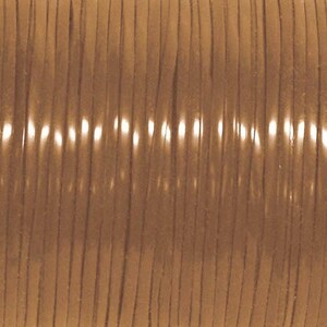 May include: A spool of light brown leather cord wound tightly in parallel vertical rows. The surface of the cord has a smooth, matte texture with subtle variations in the tan color, reflecting light along the rounded edges of each strand.