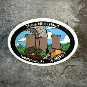 May include: Oval sticker featuring a graphic of the Three Mile Island nuclear plant with smokestacks, turtles, and a sunflower. The sticker has the text "Three Mile Island" and "Middletown, Pa" in a black border.
