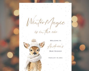 May include: A baby shower sign featuring a watercolor illustration of a fawn wearing a winter hat and scarf. The sign reads "Winter Magic is in the air" and welcomes guests to Andrea's baby shower on February 19, 20xx.