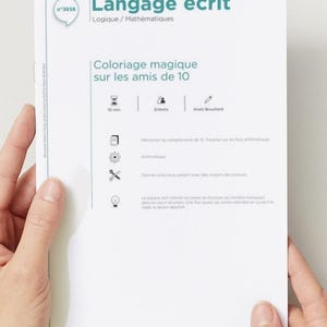 May include: A white paper titled "Langage écrit" (Written Language) with the subtitle "Logique/Mathématiques". The paper features the text "Coloriage magique sur les amis de 10" and is held by two hands.