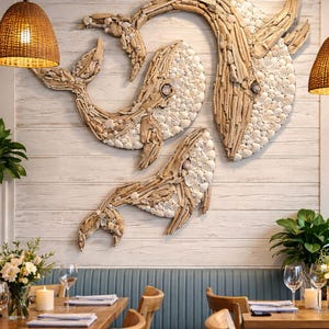 May include: A large wall art installation featuring three whales crafted from light-colored driftwood and white seashells. The whales are arranged in a swimming formation against a white horizontal wood-paneled wall, creating a textured relief.