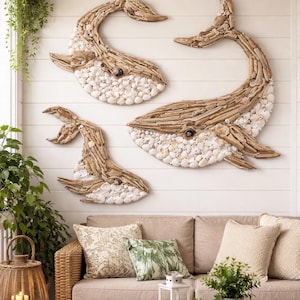 May include: Three wall art pieces shaped like whales, crafted from light brown driftwood and white seashells. The whale figures are arranged in a group, featuring textured wooden bodies and bellies covered in small, layered white shells.