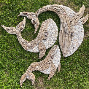 May include: Three whale-shaped wall art pieces crafted from light brown driftwood and small white seashells. The driftwood forms the outlines and structural bodies of the whales, while the white shells fill in the textured surfaces of the figures.
