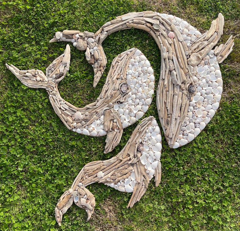 May include: Three whale-shaped wall art pieces crafted from light brown driftwood and small white seashells. The driftwood forms the outlines and structural bodies of the whales, while the white shells fill in the textured surfaces of the figures.