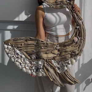 May include: A large wall sculpture shaped like a whale, constructed from various pieces of weathered driftwood and small white seashells. The driftwood forms the body and tail, while the white shells create the underbelly and eye detail.