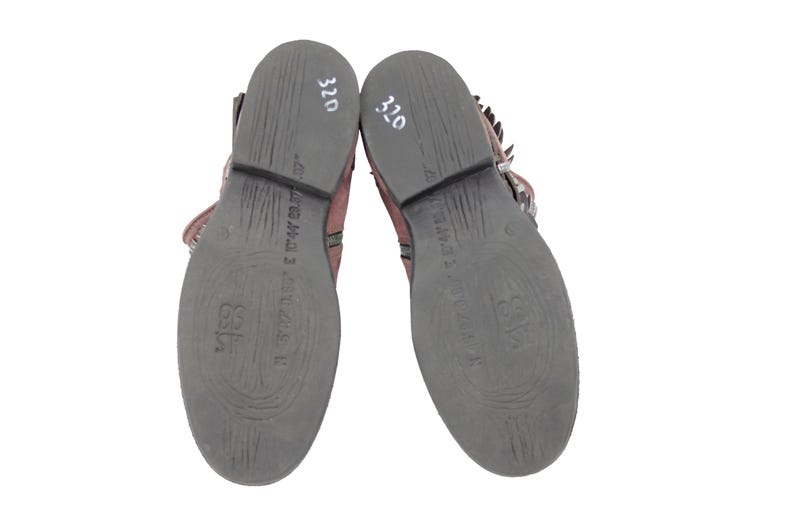 May include: Pair of brown leather ankle boots with dark gray soles. The soles have embossed patterns and text. The number "320" is written in white on the heel of each boot. The boots have buckles and fringe.