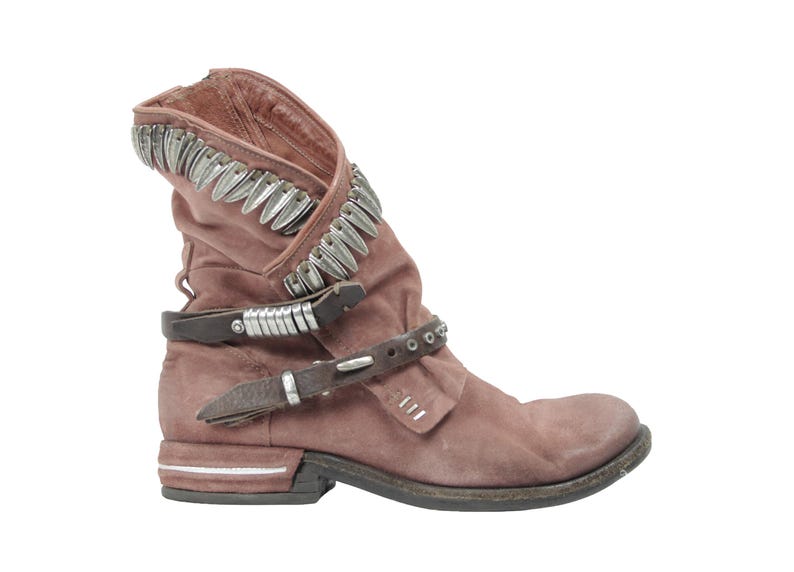May include: Dusty rose-colored ankle boot with silver-toned metal accents. The boot features a folded-over top, two brown leather straps with buckles, and a low heel. The design includes decorative metal studs.