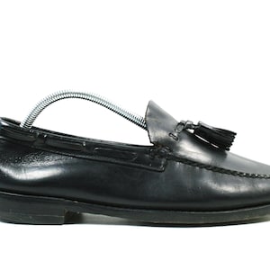 May include: Black leather loafer with a tassel detail. The shoe features a rounded toe, a low heel, and a metal shoe tree inside. The loafer is designed for comfort and style, suitable for various occasions.