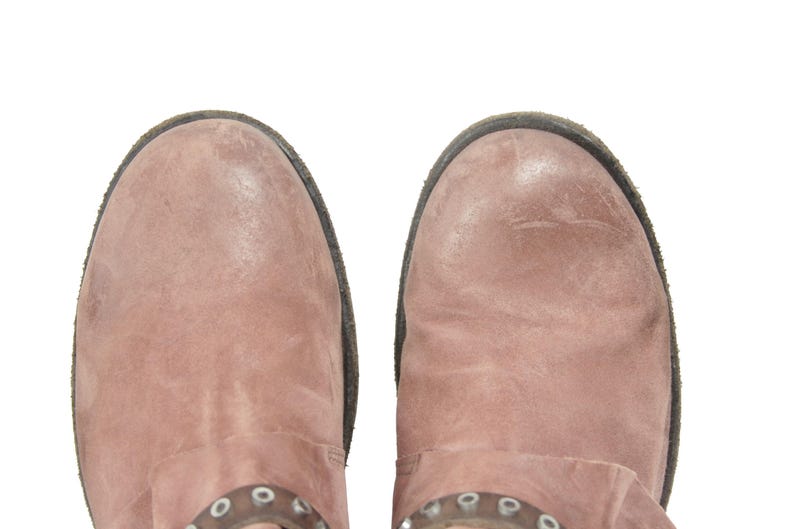 May include: Overhead shot of two dusty rose-colored leather boots. The boots have a distressed appearance with a dark brown sole and a decorative metal accent near the ankle. The boots are set against a white background.