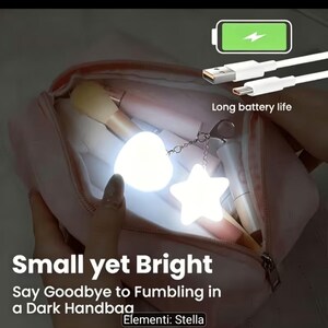May include: A light-up heart and star keychain accessory inside a pink handbag. The device emits a bright white glow and includes a white USB charging cable with the text Long battery life, Small yet Bright, Say Goodbye to Fumbling in a Dark Handbag, Elementi: Stella.