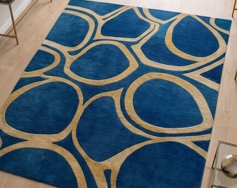 Op de afbeelding: Een rechthoekig vloerkleed met een diepblauwe achtergrond en een herhalend patroon van onderling verbonden, afgeronde, beige organische vormen. Het kleed heeft een zachte, pluizige textuur op een lichte houten vloer.