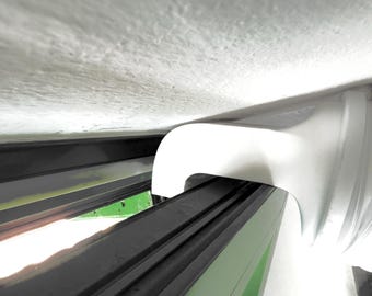 May include: A close-up view of a white, curved architectural element, possibly a part of a window frame or a similar structure. The element is positioned against a light-colored ceiling and dark-colored frame.