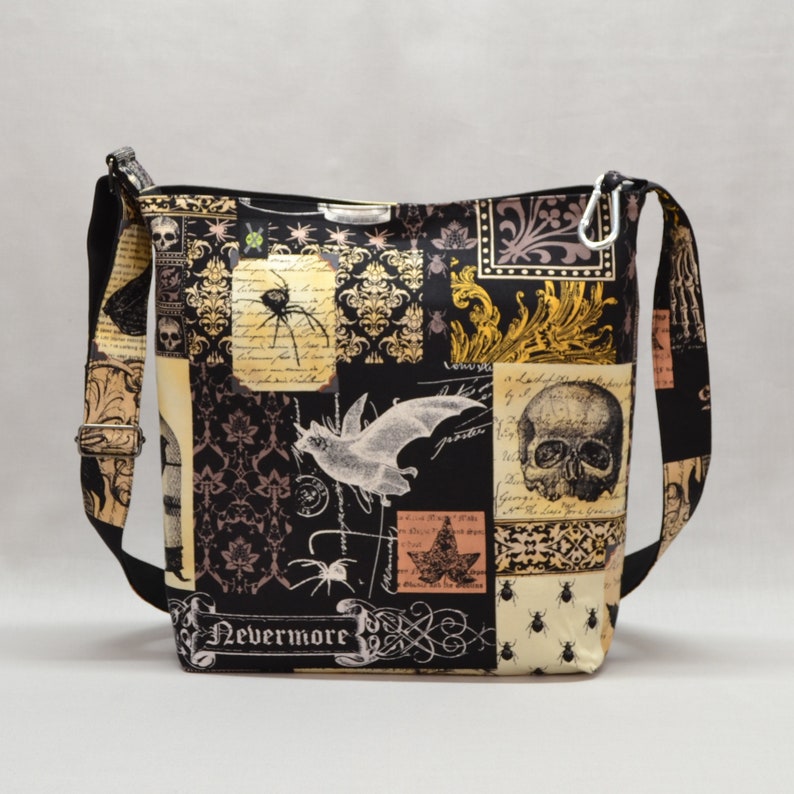 Pode incluir: Bolsa transversal preta e bege com um design de patchwork com caveiras, morcegos, aranhas e padr&otilde;es ornamentados. A bolsa tem uma al&ccedil;a preta ajust&aacute;vel e um fecho prateado. O texto "Nevermore" &eacute; vis&iacute;vel.