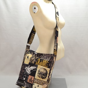 Pode incluir: Bolsa de ombro preta e bege com um design de patchwork com caveiras, morcegos e insetos. A bolsa tem uma al&ccedil;a longa e a palavra "Nevermore" est&aacute; impressa na parte inferior. Uma gargantilha preta com tachas est&aacute; em volta do pesco&ccedil;o do manequim.