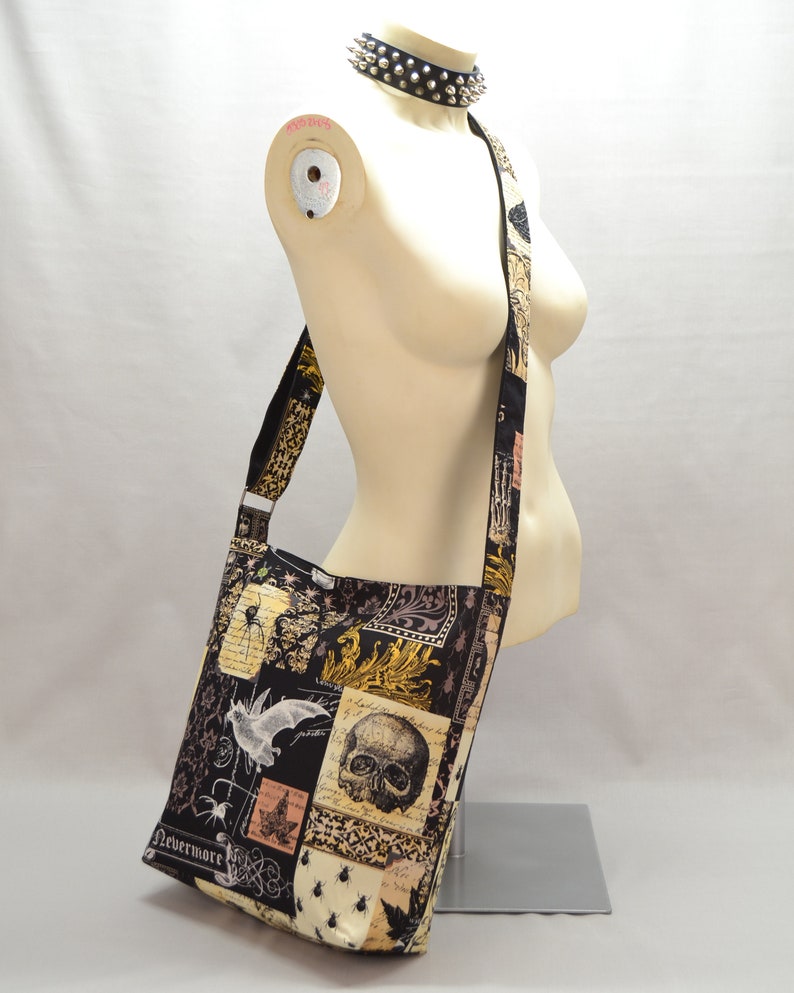 Pode incluir: Bolsa de ombro preta e bege com um design de patchwork com caveiras, morcegos e insetos. A bolsa tem uma al&ccedil;a longa e a palavra "Nevermore" est&aacute; impressa na parte inferior. Uma gargantilha preta com tachas est&aacute; em volta do pesco&ccedil;o do manequim.