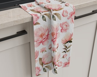 May include: A white kitchen towel with a pink floral pattern. The towel is folded and hanging on a kitchen counter.