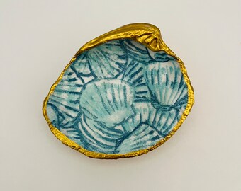 May include: A blue and white seashell-shaped dish with a gold rim. The dish is decorated with a pattern of seashells.