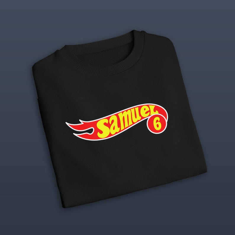 K&ouml;nnte beinhalten: Schwarzes Sweatshirt mit einem rot-gelben Aufdruck "Samuel 6". Das Design ist in einer stilisierten Schriftart gehalten, &auml;hnlich einem Spielzeugauto-Logo. Das Sweatshirt ist aus weichem Material.
