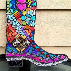May include: A colorful mosaic cowboy boot with pink hearts, turquoise, and gold accents. The boot is made of small pieces of glass and tile.