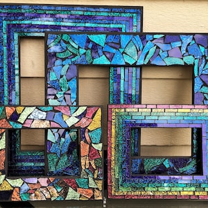 Puede incluir: Cuatro marcos de fotos de mosaico con marco negro con piezas de vidrio de diferentes colores. Los marcos están anidados uno dentro del otro, creando un efecto de capas. Las piezas de vidrio son iridiscentes y reflejan la luz en una variedad de colores, incluyendo azul, verde, morado y rosa.