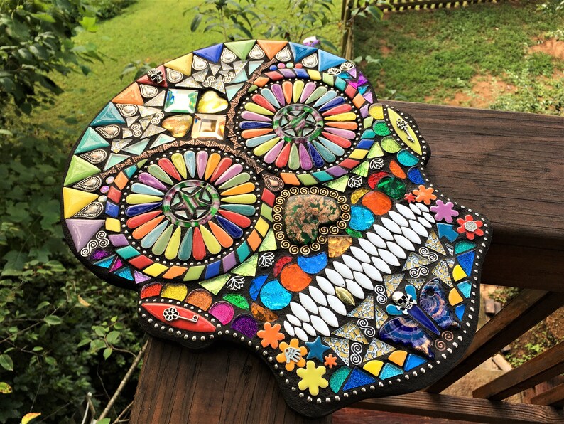 May include: A colorful mosaic skull, featuring a variety of shapes and colors. The mosaic includes triangles, squares, and other geometric forms in shades of blue, orange, yellow, and green. The skull is a decorative piece, likely for home decor.