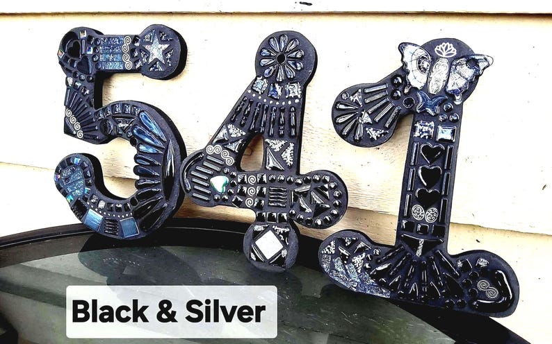 three black and silver mosaic letters on a wall, with the text "Black & Silver" below them.