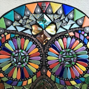 May include: A colorful mosaic skull design with a black background. The mosaic features a variety of shapes and colors, including triangles, diamonds, and teardrops. The design incorporates a star in the eye sockets and a small skull at the top.