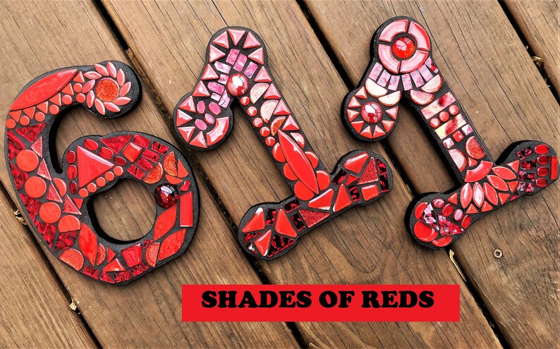 Może przedstawiać: Trzy mozaikowe numery dom&oacute;w, 611, wykonane z czerwonych i r&oacute;żowych płytek. Numery znajdują się na drewnianym tle. Tekst "SHADES OF REDS" znajduje się pod numerami.