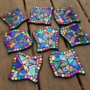 K&ouml;nnte beinhalten: Neun bunte Mosaik-Untersetzer mit geometrischem Design. Jeder Untersetzer zeigt eine andere Anordnung von schillernden Glasst&uuml;cken in Blaut&ouml;nen, Gr&uuml;n, Lila, Rosa und Gold.