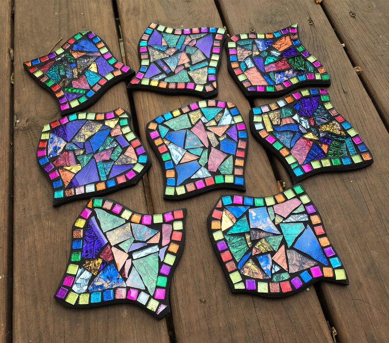 K&ouml;nnte beinhalten: Neun bunte Mosaik-Untersetzer mit geometrischem Design. Jeder Untersetzer zeigt eine andere Anordnung von schillernden Glasst&uuml;cken in Blaut&ouml;nen, Gr&uuml;n, Lila, Rosa und Gold.