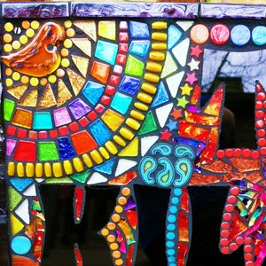 May include: A colorful mosaic artwork featuring a bird, geometric shapes, and a stylized cat. The mosaic uses a variety of glass tiles in shades of red, orange, yellow, green, blue, and purple. The background is black, and the piece is framed.