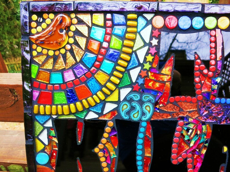 May include: A colorful mosaic artwork featuring a bird, geometric shapes, and a stylized cat. The mosaic uses a variety of glass tiles in shades of red, orange, yellow, green, blue, and purple. The background is black, and the piece is framed.