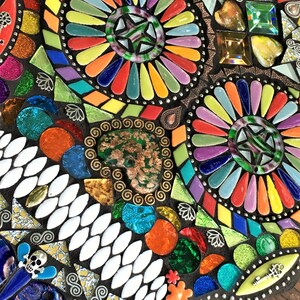 May include: A colorful mosaic art piece with a dark background. The mosaic features a variety of shapes and colors, including red, orange, yellow, green, blue, and purple. The design includes circular patterns and decorative elements.