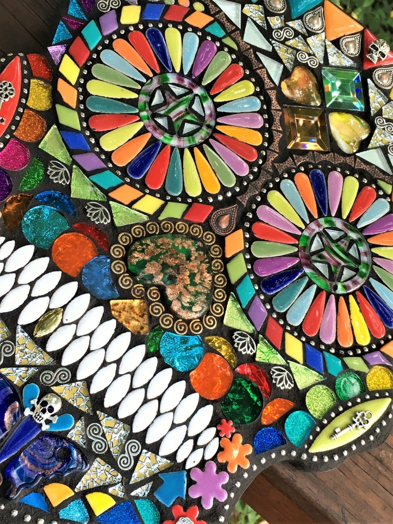 May include: A colorful mosaic art piece with a dark background. The mosaic features a variety of shapes and colors, including red, orange, yellow, green, blue, and purple. The design includes circular patterns and decorative elements.