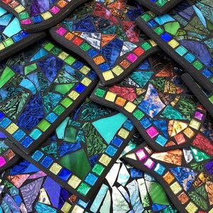 K&ouml;nnte beinhalten: Ein Stapel bunter Mosaik-Untersetzer mit schwarzem Rand. Die Untersetzer bestehen aus kleinen Glassplittern in Blaut&ouml;nen, Gr&uuml;n, Rot und Gelb.