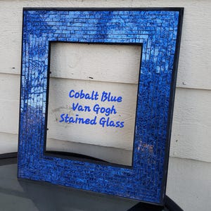 May include: A square cobalt blue stained glass frame with a black border. The frame is made of small, rectangular pieces of glass arranged in a mosaic pattern. Text on the frame reads "Cobalt Blue Van Gogh Stained Glass."