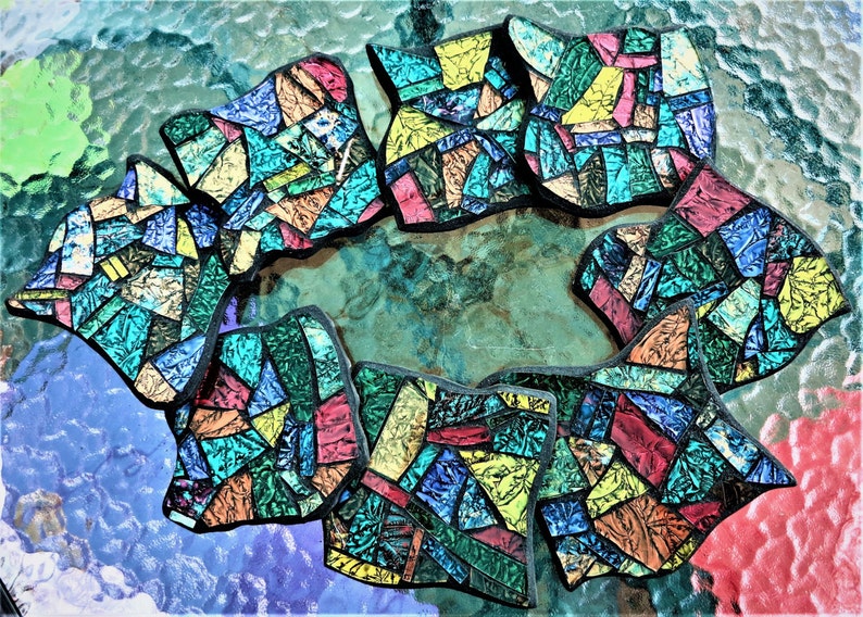K&ouml;nnte beinhalten: Ein Set aus acht bunten Mosaik-Untersetzern mit geometrischem Design. Die Untersetzer bestehen aus kleinen Glassplittern in Blaut&ouml;nen, Gr&uuml;nt&ouml;nen, Gelb, Rot und Orange.